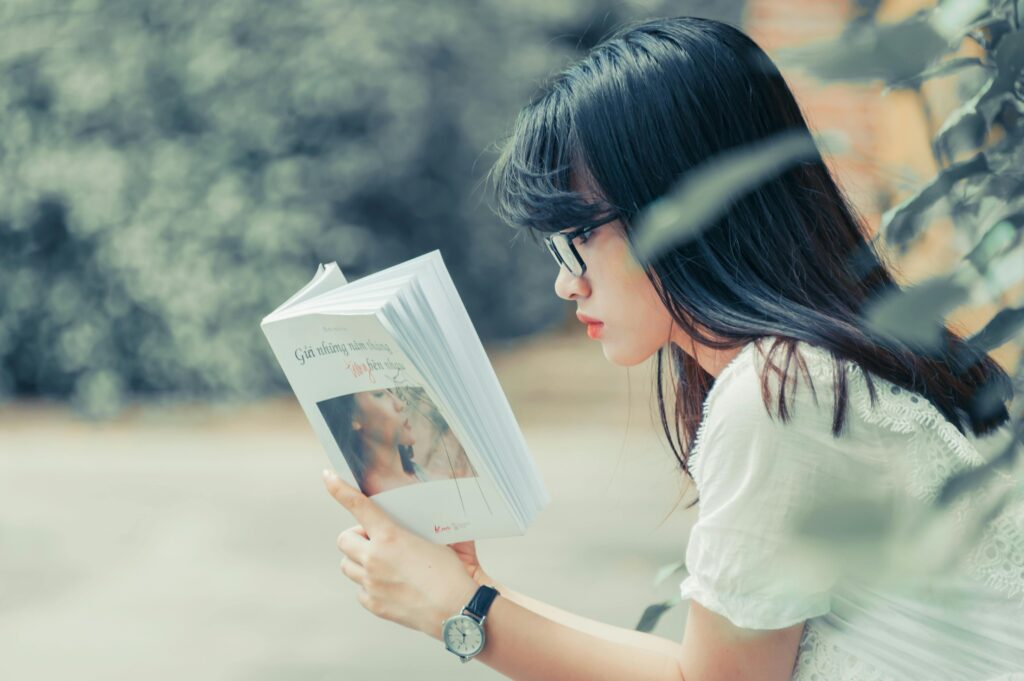 Asian woman reading a book in summer. Relaxed outdoor setting with focus on leisure and education.
